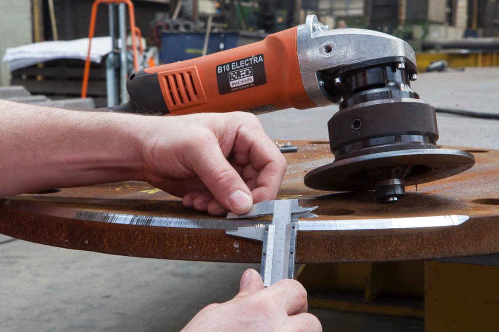 Töölise käed materjali mõõtmas, taga paistab faasimasin B10 Electra