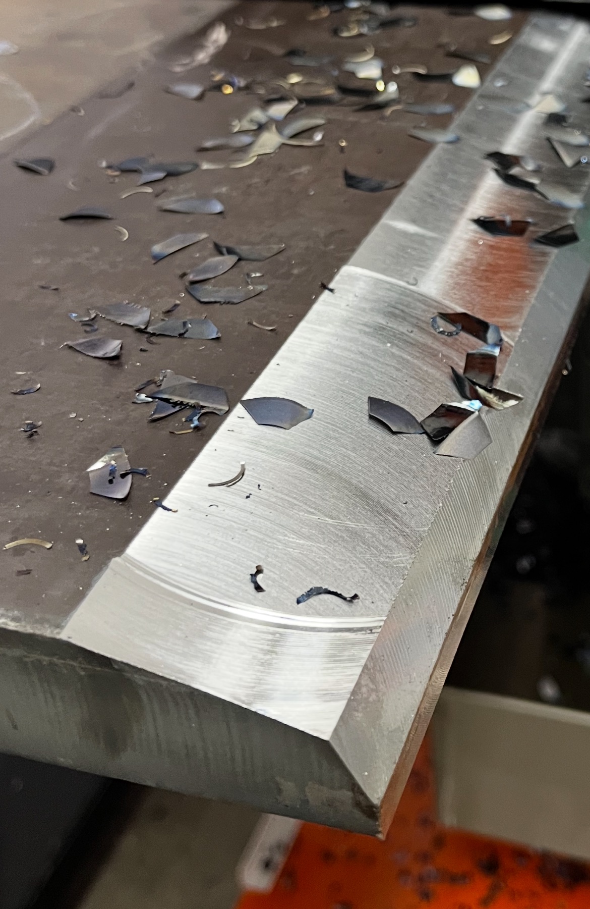 Lähivõte töödeldud metallservast, mille ümber on hajunud metallilaastud, esitledes faasitud lõiget.